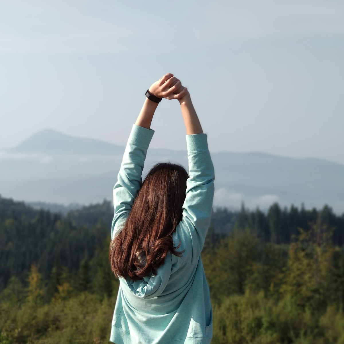 woman in teal long sleeve shirt standing on top of mountain during daytime